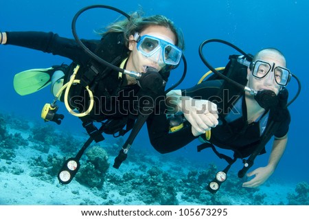 romantic couple scuba dive together in the ocean on a coral reef
