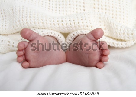 Close up of two small newborn baby boy feet with heels touching covered by a cream cotton blanket