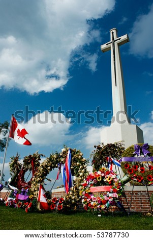 Marble Cross at war memorial with flowers and Canadian flag under blue sky