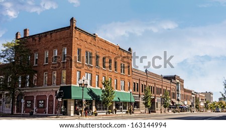 A photo of a typical small town main street in the United States of America. Features old brick buildings with specialty shops and restaurants. Decorated with autumn decor.