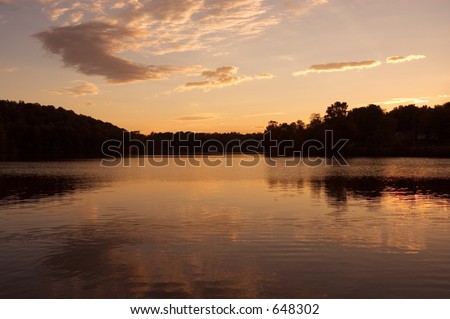 Beautiful colors and reflections as the sun sets over the trees on a calm lake.