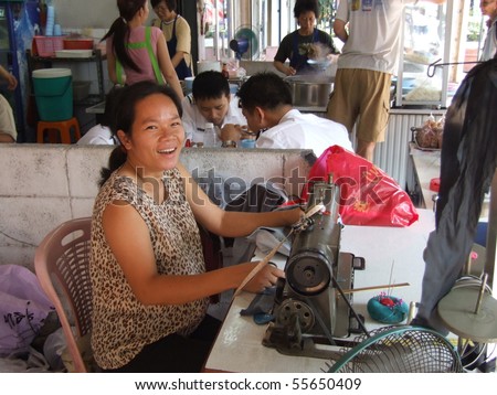 BANGKOK, THAILAND - APRIL 03: Thai woman sits by the roadside making clothes with a sewing machine. April 03 2007 in Bangkok.