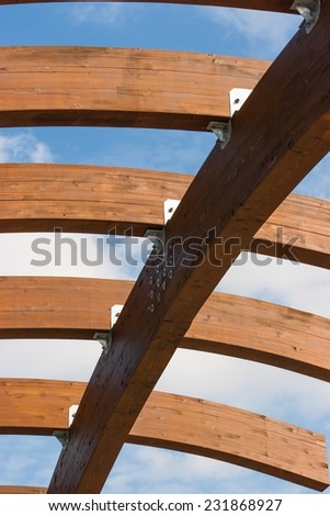Timber frame arch against blue sky and white clouds midday underneath view.