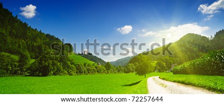 Idyllic countryside panoramic view. Green meadow, hills, field and road under blue sky in sun rays. Slovenia.