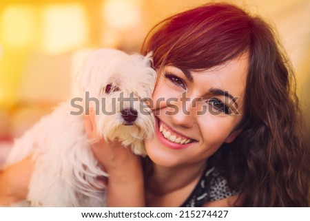 Beautiful happy woman with a joyful loving smile cuddling her pet dog, a curly haired white toy breed with a cute little face