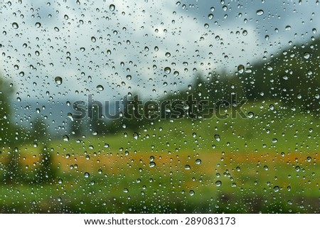 View of the mountain landscape with forest, meadow and flowers through the window glass of the car covered by rain drops