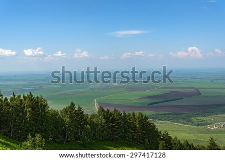 Scenic top view on the town, trees, forest, agricultural fields, farms and villages on the background of blue sky and clouds in summer