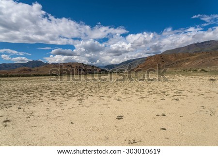 Scenic desert steppe landscape with mountains. Dry land with rare plants as the foreground and mountains, sky and clouds in the background.