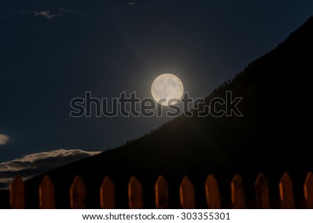 Night landscape with the moon and clouds in the sky against the dark outline of mountains