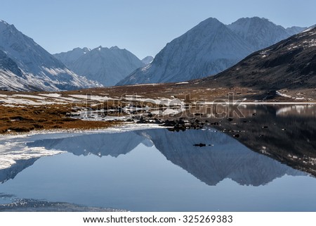 Scenic mountain autumn landscape with a lake, mountains reflecting in the lake, with snow and ice on the shore on a sunny day