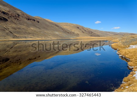 Bright picturesque mountain autumn landscape with a lake, mountains reflecting in the lake, with snow on the banks and a cloud against the blue sky on a sunny day