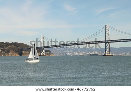 White sailboat on sunny day, with island and bridge as background