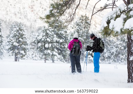 Hiking Break (Couple hiking in snowshoes take a break under a tree)