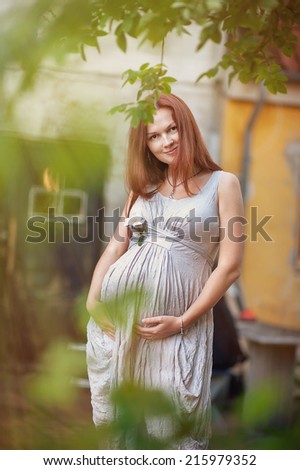 portrait of pregnant woman, close up, grey dress, with flower in the hand, smile, hands on belly