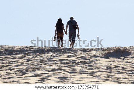 Young couple walks on sand dune. Fingal Bay. Port Stephens. Australia.
