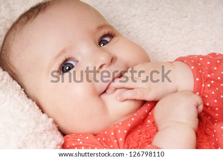 Close-up portrait of beautiful smiling baby girl with hand near the face lying on blanket, studio shot