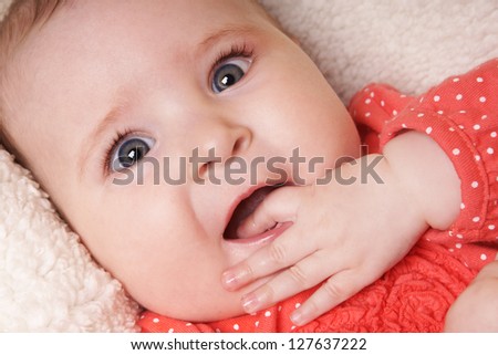 Close-up portrait of beautiful smiling newborn baby girl with fingers in mouth, studio shot