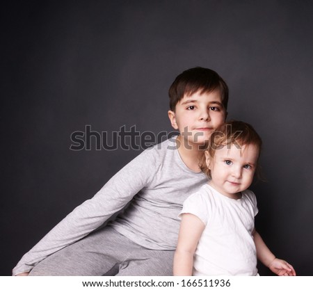 Beautiful happy kids: smiling young brother and and laughing baby sister in a hug, studio shot