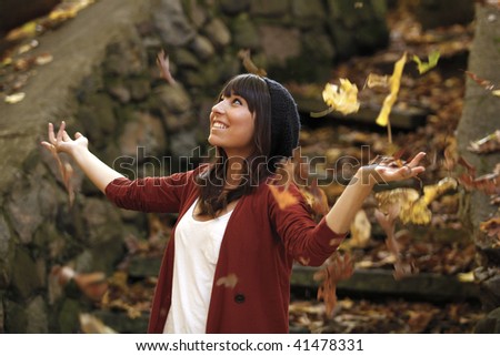 Girl with her arms raised looking up with leaves falling. Shot in front of a large stone stairway.