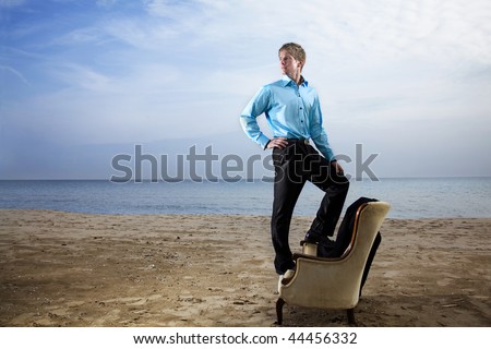 A young man in a suit on the beach with a vintage chair.