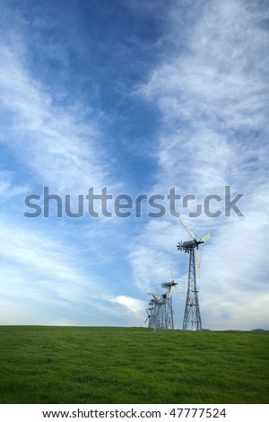 Windmills together in a grassy hilly area around sunset.