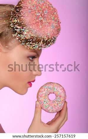 Beautiful woman with donut on head and in hand on pink background