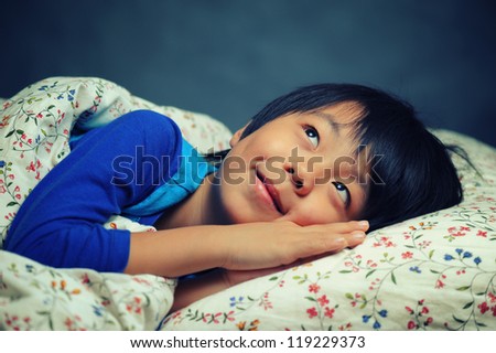 Happy Asian boy lying in bed and preparing to go to sleep