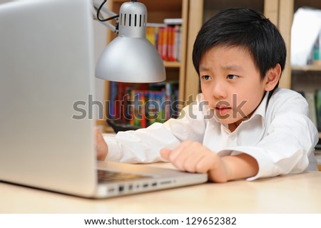 Frustrated school boy in white shirt looking at laptop computer