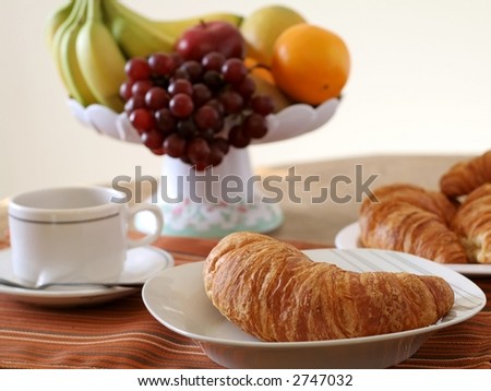 Breakfast table set with fresh croissants, coffee and fruit bowl