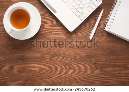 Office table with notepad, computer, pen and tea cup
