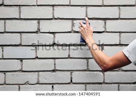 hand holding a graffiti spray can in front of a brick wall