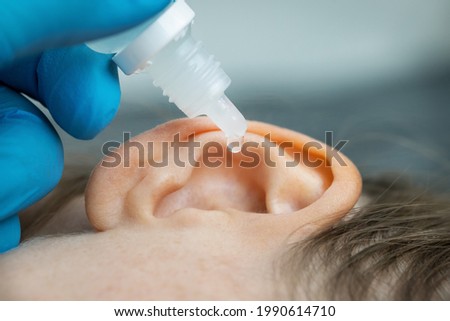 doctor dripping ear drops into patient ear. ear pain and clogged ears concept