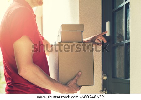 delivery service courier ringing the house doorbell with boxes in hands