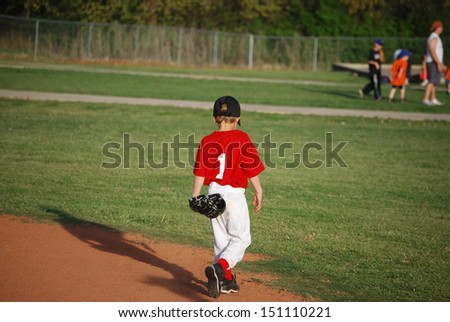 Little league youth baseball player walking on field.