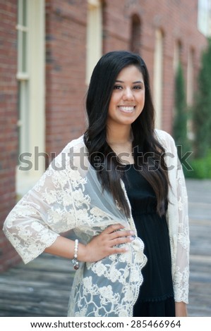 Beautiful and happy senior graduate standing in front of building wearing a dress.