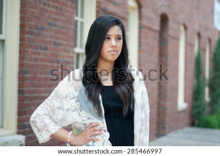 Beautiful and sad senior graduate standing in front of building wearing a dress.