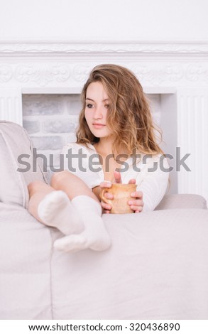 Toned portrait of a beautiful and sexy young adult attractive dreaming  woman in beige sweater and vanilla socks sitting on the beige armchair in the white room.