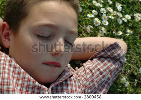 Young child relaxing in the garden, biting his lip