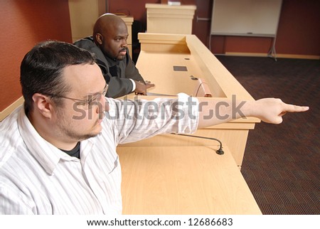 Man on the witness stand pointing out someone to the judge