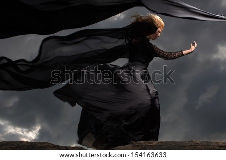 Wind blowing blond hair and black dress of the young girl standing on the mount