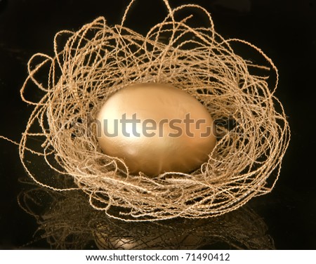 Gold egg in a nest from gold threads on a black background with reflection. Against a gold dust