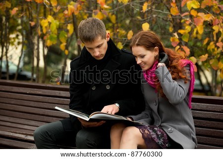 young couple on bench in autumn park and read book