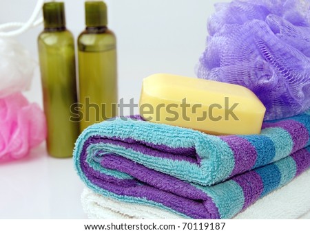 A Nice Bath Scene with Fluffy Blue and Purple Striped Towels, a Bar of Yellow Soap, Shampoo Bottles and Body Scrubbers
