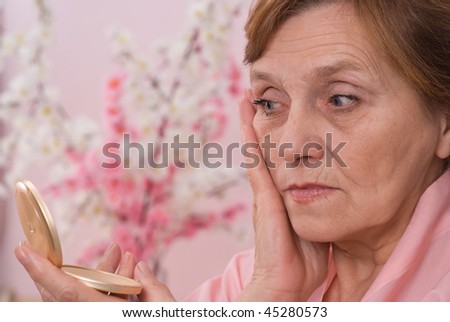 elderly woman looking at  face in the mirror