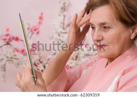 elderly woman with a mirror on a pink background