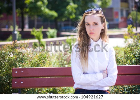 Sad office worker (woman) sits in the park and looks into the camera. Outdoor