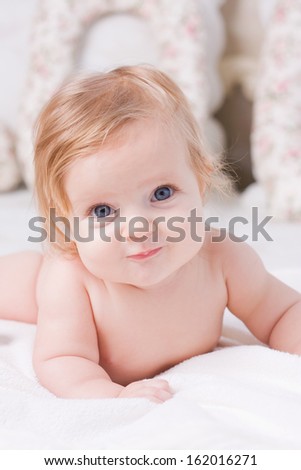 Cute little baby with big blue eyes  lies down on the bed, smile and looks towards