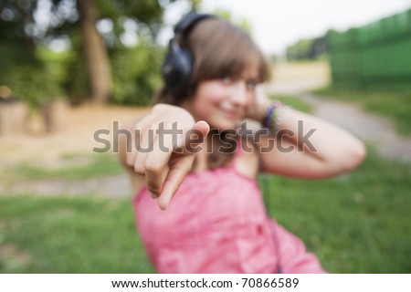 beautiful teenage girl in a pink dress with headphones to point the finger at the camera, focus on finger