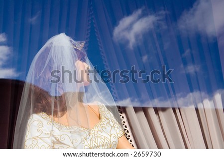 A blue sky with some clouds are reflected off the window of a bridal store.