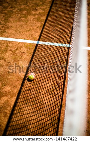 abstract: tennis ball and net with great shadows on court